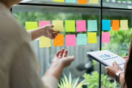 Business colleague reading financial budget document to discussion and writing ideas in sticky note.の写真素材