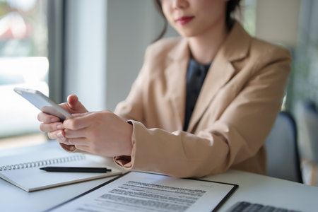 Businesswomen using smartphone to researching data about new business and analysis strategy investment for management about new startup project while checking financial data on document in workplace.の写真素材