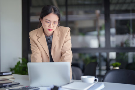 Businesswomen wearing glasses and reading business report to checking finance chart data on laptop for analysis strategy investment and management about new startup project while working in workplace.の写真素材