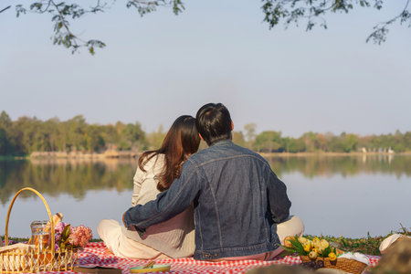 Young couple in love sitting on blanket with picnic basket and embracing to watching lake view.の写真素材