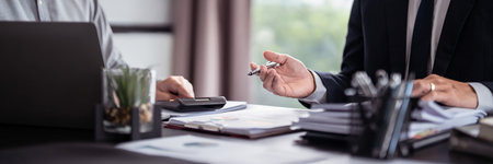 Two businessman real estate seller use calculator to calculating and brainstorming about property investment while explaining document term data about home sales contract and home insurance in office.の写真素材