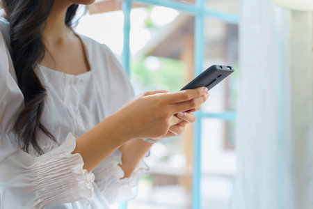 Closeup hands of young asian businesswoman use smartphone to chat texting message and checking email after analysis strategy about investment and planning of new startup project while working in cafe.の写真素材
