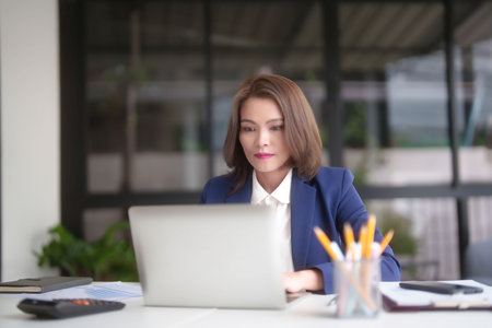 Asian businesswomen reading marketing business report and financial chart to typing business data on keyboard laptop while analyze investment and market stock of new startup in outside office.の写真素材