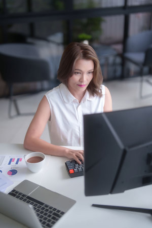 Asian businesswomen typing business information on keyboard to working about planning of marketing business report on computer while analyze investment and market stock of new startup in workplace.の写真素材
