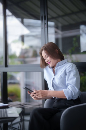 Asian businesswomen using smartphone to researching business information and reading marketing report while working to analyzing investment and market stock of new startup in outside workplace.の写真素材