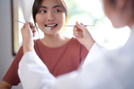 Asian dentist doctor women using explorer mirror tool to examining teeth of patient and explaining about oral dental treatments while discussion about dental health and healthcare in dental clinic.の写真素材