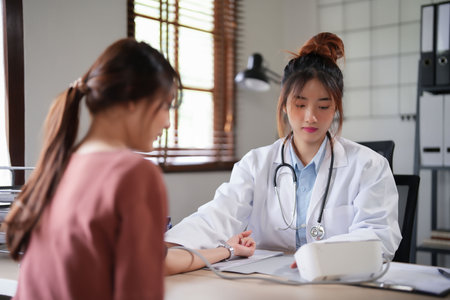 Asian psychologist women using digital sphygmomanometer to checking blood pressure and heart rate of female patient while giving to counseling about medicine and mental health therapy in clinic.の写真素材