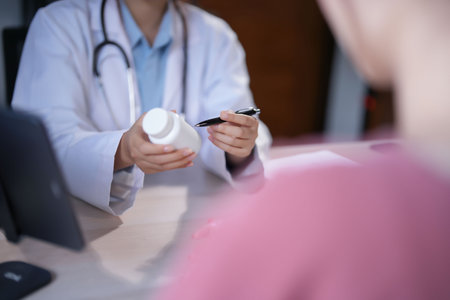 Asian psychologist women pointing on pills bottle to explaining medicine and prescription to female patient while giving counseling about medical and mental health therapy to female patient in clinic.の写真素材