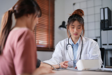 Asian psychologist women using digital sphygmomanometer to checking blood pressure and heart rate of female patient while giving to counseling about medicine and mental health therapy in clinic.の写真素材