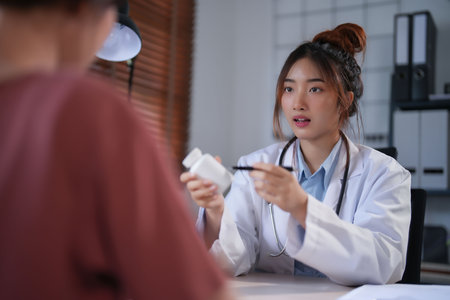 Asian psychologist women showing pills bottle to explaining medicine and prescription to female patient while giving counseling to explaining about mental health therapy to female patient in clinic.の写真素材