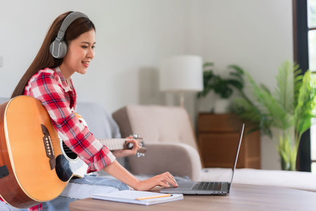 Guitar and singer concept, Young asian woman playing acoustic guitar while learning music on laptop.の写真素材