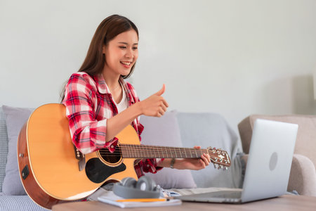 Hobby concept, Young asian woman playing acoustic guitar on live stream and doing thumbs up gesture.の写真素材