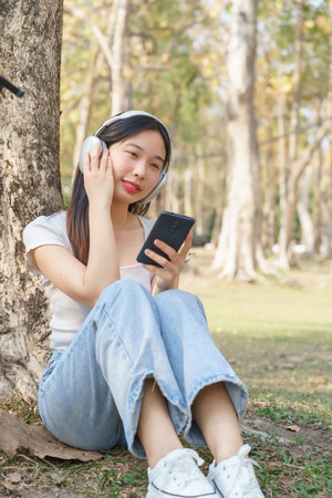 Young asian women wearing headphone and holding smartphone to listening audio music with happiness while sitting on grass to relaxation with journey travel lifestyle after cycle bicycle in the park.の写真素材