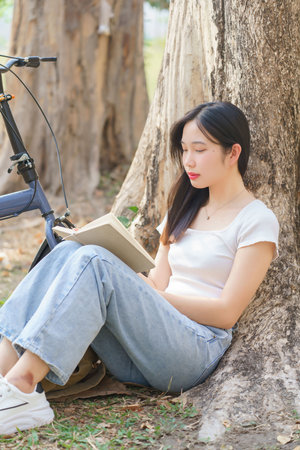 Young asian women sitting on grass to leaning the tree and reading a book with recreation happiness while relaxation with journey travel trip lifestyle after cycle bicycle in the nature park.の写真素材