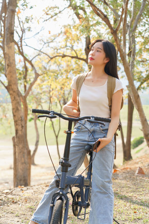 Young asian women with backpack sitting on bicycle and holding smartphone to enjoying with nature view while relaxation with journey travel for healthy lifestyle after cyclist bicycle in the park.の写真素材