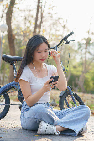 Young asian women wearing earphone to listening audio music and watching entertainment on smartphone with happiness while relaxation with journey travel lifestyle after cycling bicycle in the park.の写真素材