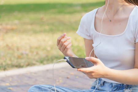 Closeup of young asian women wearing earphone and listening music on smartphone with happiness while sitting on the street to relaxation with journey travel lifestyle after cycling bicycle in park.の写真素材