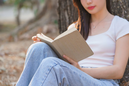 Young asian women sitting on grass to leaning the tree and reading a literature book with recreation happiness while enjoying to relaxation with journey travel trip lifestyle in the nature park.の写真素材