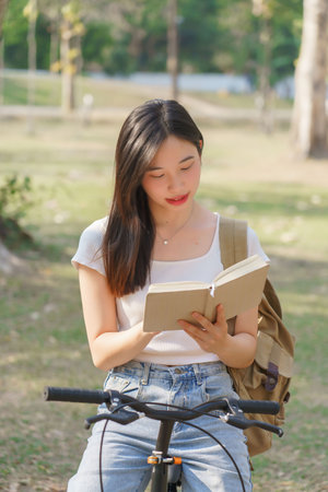 Young asian women with backpack sitting on bicycle and reading a book with happiness to resting after cycling bicycle in the nature park while relaxation with journey travel for healthy lifestyle.の写真素材