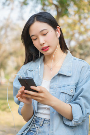 Close up of young asian women wearing earphone and using smartphone to listening music and chatting while sitting on bicycle to relaxation with journey travel lifestyle after cycling bicycle in park.の写真素材