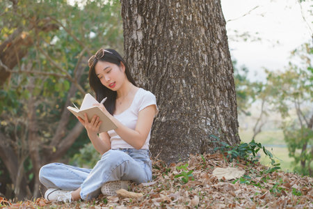 Young asian women sitting on grass under the tree to writing business data and journey dairy in notebook while enjoying and happiness to relaxation with journey travel lifestyle in the nature park.の写真素材