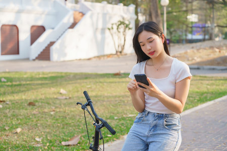 Young asian women sitting on bicycle to reading message chat and checking social media on smartphone after cycling bicycle in the park while relaxation with journey travel lifestyle for healthy.の写真素材