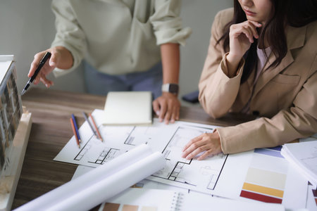 Two female architects discuss and brainstorm about building model and interior design on blueprint.