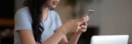 Asian teenage student woman using smartphone to chatting with friends and doing assignment homework after watching lecture video online lesson on laptop and studying about education knowledge in cafe.の写真素材