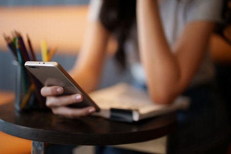 Asian teenage student woman using smartphone to surfing social media and entertainment for relaxation after studying and reading information in paperwork to learning about education knowledge in cafe.の写真素材