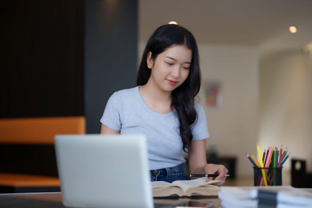 Asian teenage student woman reading a book and writing notes to doing homework while watching...