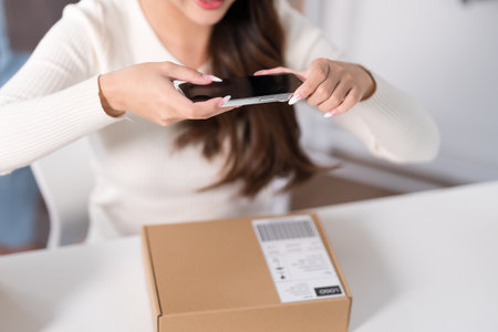A woman photographs a product on a desk in a workspace filled with shipping boxes and clothing racks.の写真素材