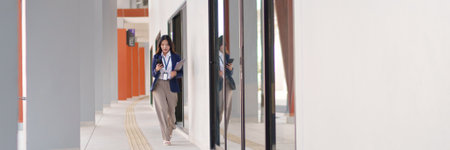 Young Asian businesswoman walking outdoors while checking her smartphone with a focused expressionの写真素材