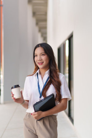 Young Asian businesswoman walking confidently outdoors with coffee and documents in handの写真素材