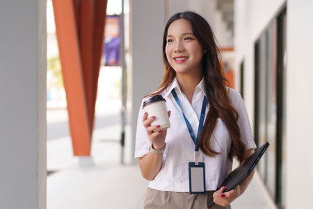 Young Asian businesswoman walking confidently outdoors with coffee and documents in handの写真素材