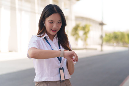 Asian businesswoman checking time on her smartwatch while standing outdoors in a modern business areaの写真素材