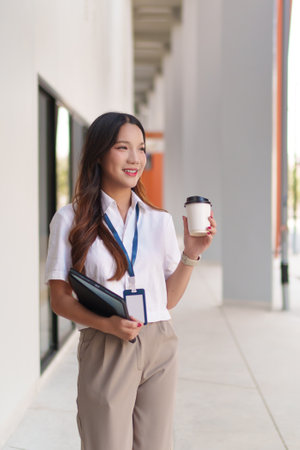 Young Asian businesswoman walking confidently outdoors with coffee and documents in handの写真素材