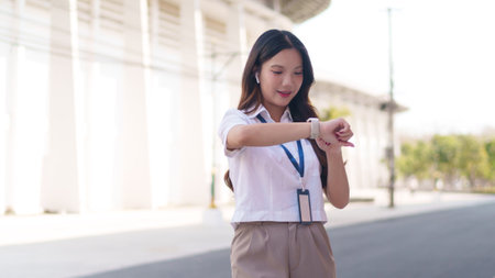 Asian businesswoman checking time on her smartwatch while standing outdoors in a modern business areaの写真素材