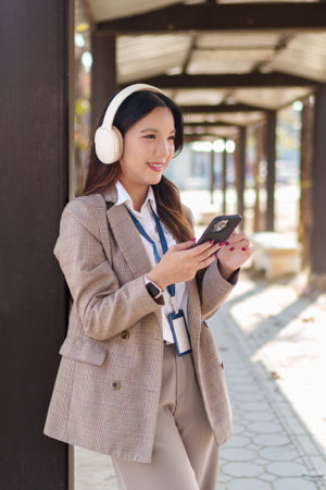 Young Asian businesswoman putting on wireless headphones and enjoying music in an outdoor walkwayの写真素材