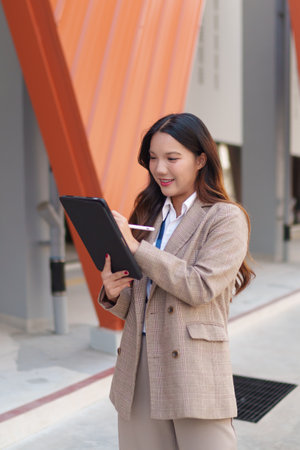 Asian businesswoman working on a tablet while standing outside a modern office buildingの写真素材
