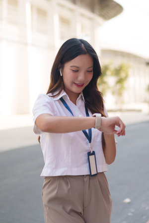 Asian businesswoman checking time on her smartwatch while standing outdoors in a modern business areaの写真素材