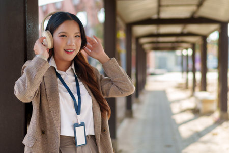 Young Asian businesswoman putting on wireless headphones and enjoying music in an outdoor walkwayの写真素材