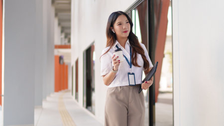 Young Asian businesswoman walking confidently outdoors with coffee and documents in handの写真素材
