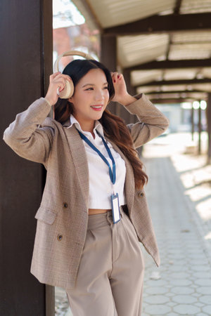 Young Asian businesswoman putting on wireless headphones and enjoying music in an outdoor walkwayの写真素材