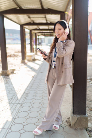 Young Asian businesswoman putting on wireless headphones and enjoying music in an outdoor walkwayの写真素材
