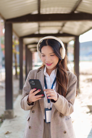 Young Asian businesswoman putting on wireless headphones and enjoying music in an outdoor walkwayの写真素材