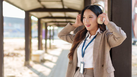 Young Asian businesswoman putting on wireless headphones and enjoying music in an outdoor walkwayの写真素材