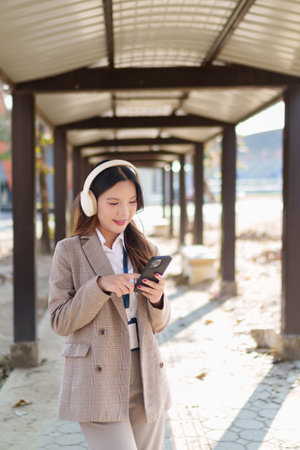 Young Asian businesswoman putting on wireless headphones and enjoying music in an outdoor walkwayの写真素材