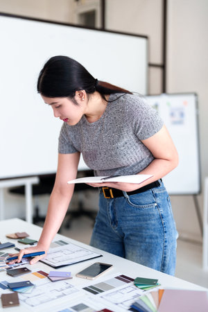 Young architect selecting materials and color swatches while standing at modern interior design workstationの写真素材