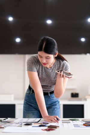 Interior designer discussing project on phone while reviewing material palette in modern workspaceの写真素材