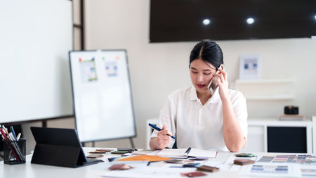 Interior designer making business call while working on color and material selection at design studio deskの写真素材